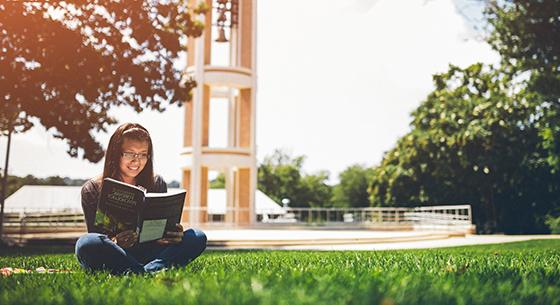 Photo of Hispanic girl reading a book on the bell tower quad